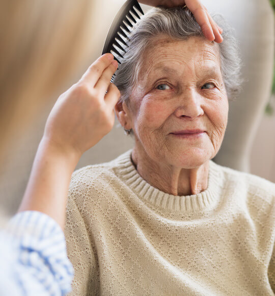 Eine Angehörige kämmt einer lächelnden Seniorin die Haare